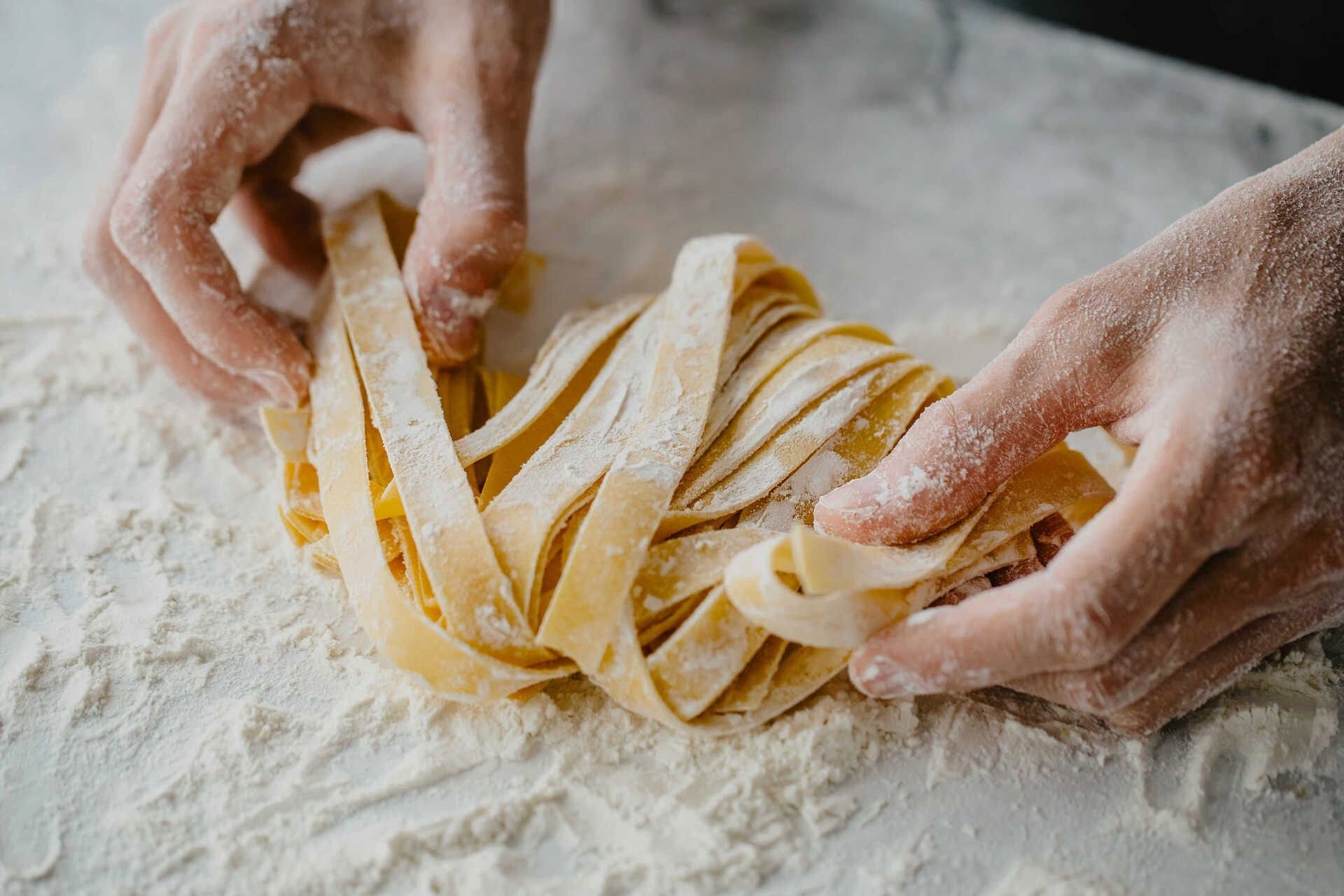 Eine Person hält ein Stück Pasta auf einem Tisch
